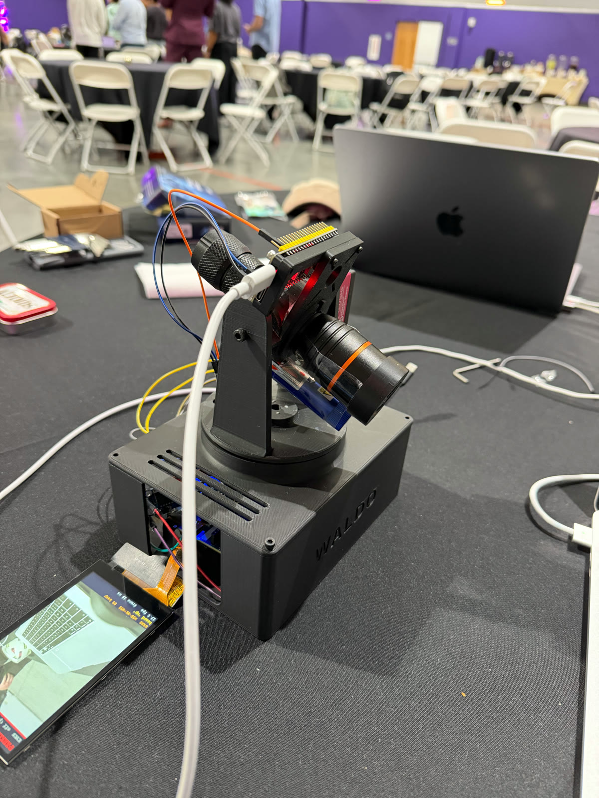 WALDO, a pan-tilt camera tracker: a black 3D-printed base embossed with 'WALDO' carrying a motorised camera head, with a small screen showing the live camera feed.